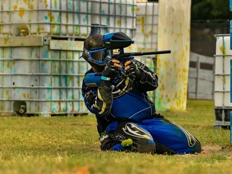 Παίκτης paintball γονατιστός πίσω από εμπόδιο